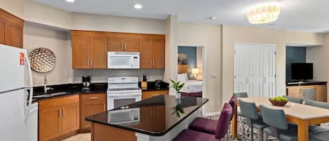 A modern kitchen with wooden cabinets, a central island, and a dining area with purple chairs.