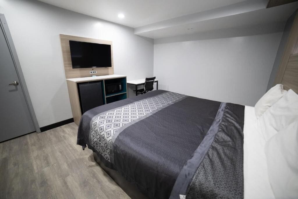 A hotel room with a bed, a desk, a chair, a television, and a wardrobe.
