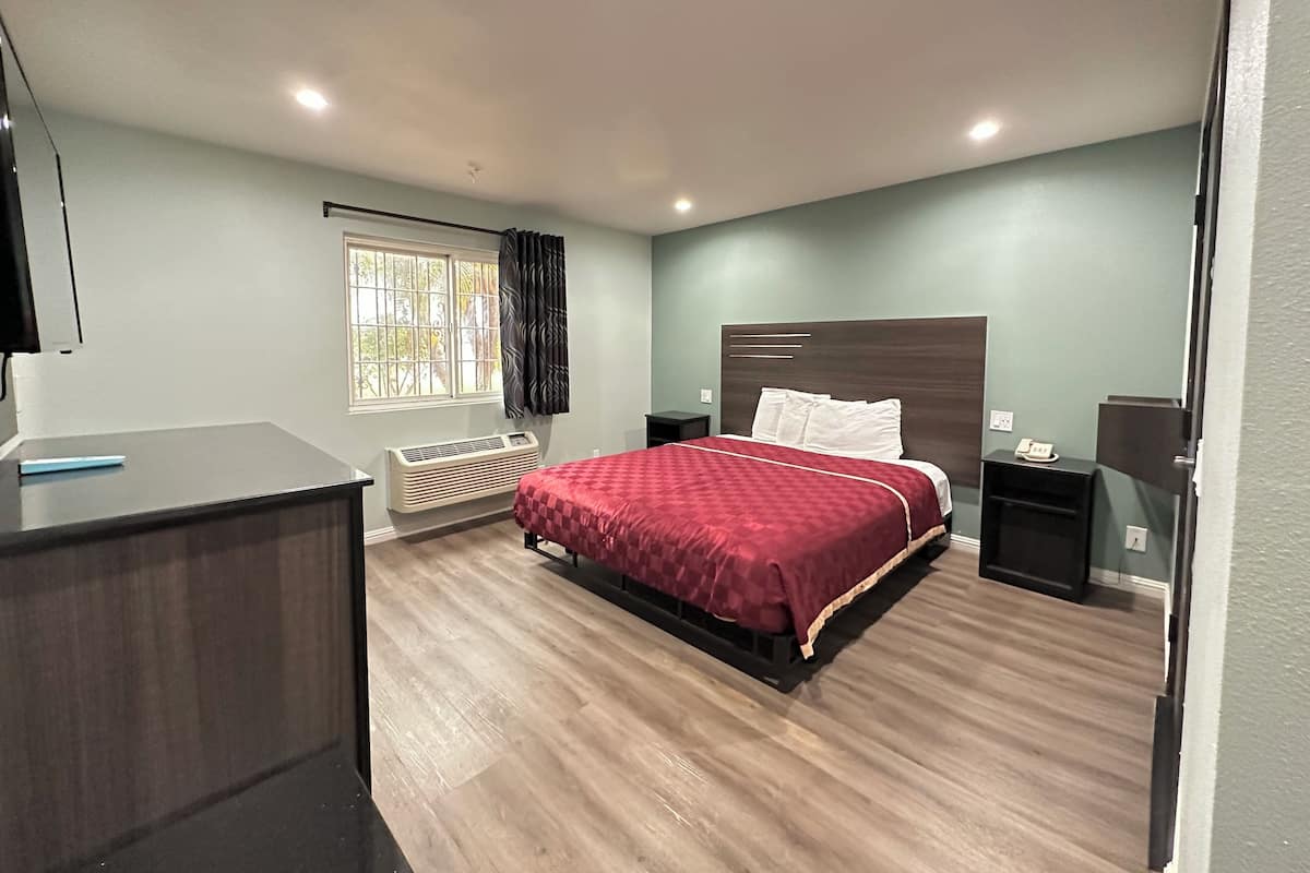A bedroom with a bed, bedside tables, a desk, a window, and an air conditioning unit.