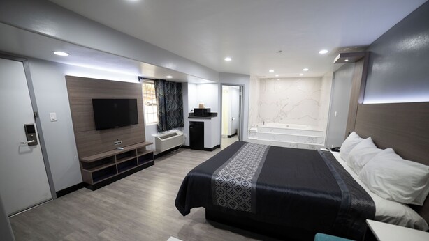 Une chambre d’hôtel moderne dotée d’un grand lit, d’un téléviseur à écran plat, d’un système de climatisation intégré, d’un petit coin salon et d’une baignoire.