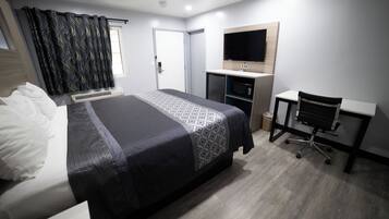 Una habitación de hotel moderna con una cama grande, un escritorio con silla, un televisor de pantalla plana montado en la pared y una ventana con cortinas.