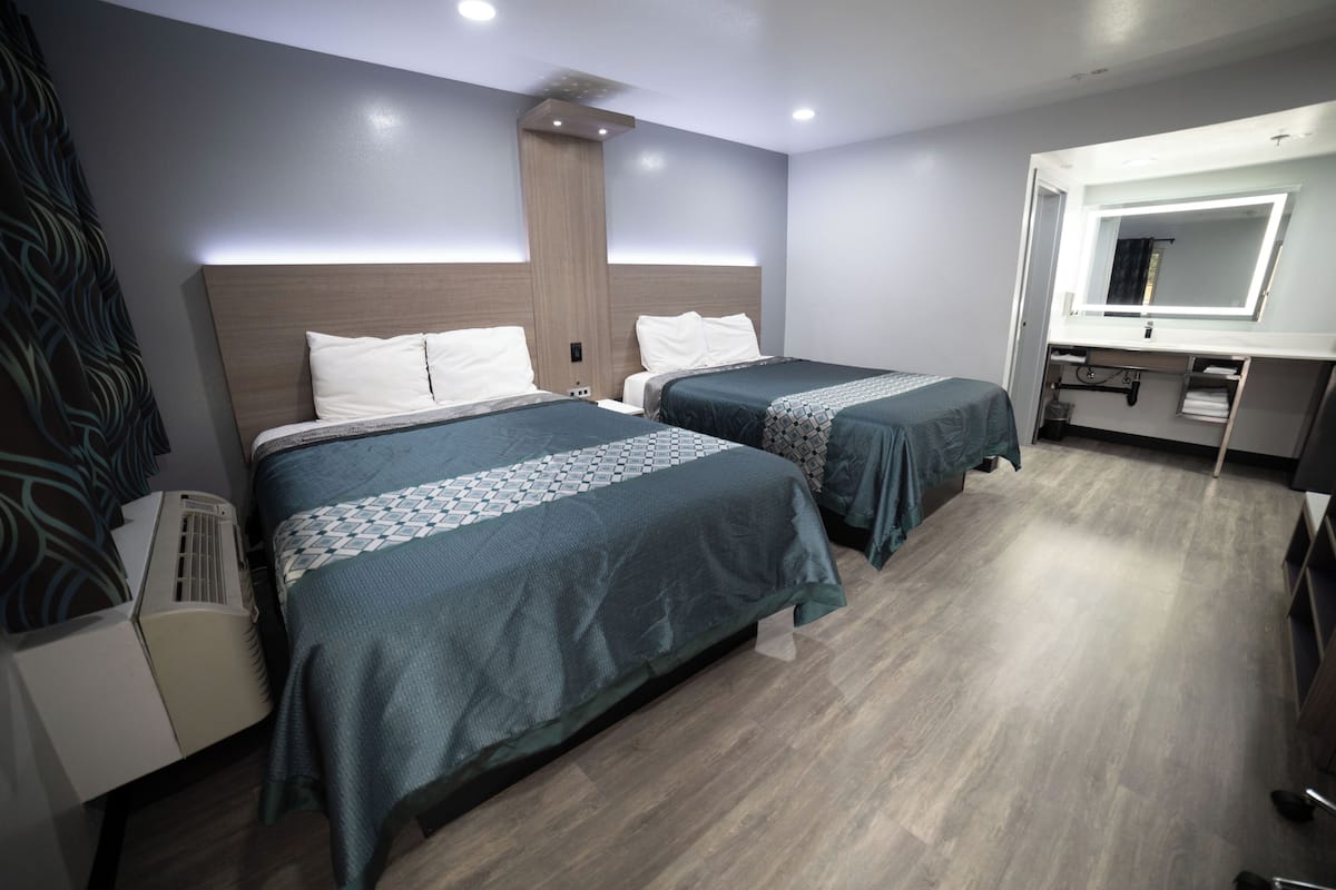 A hotel room with two beds, a large mirror, a vanity, and a ceiling fan.