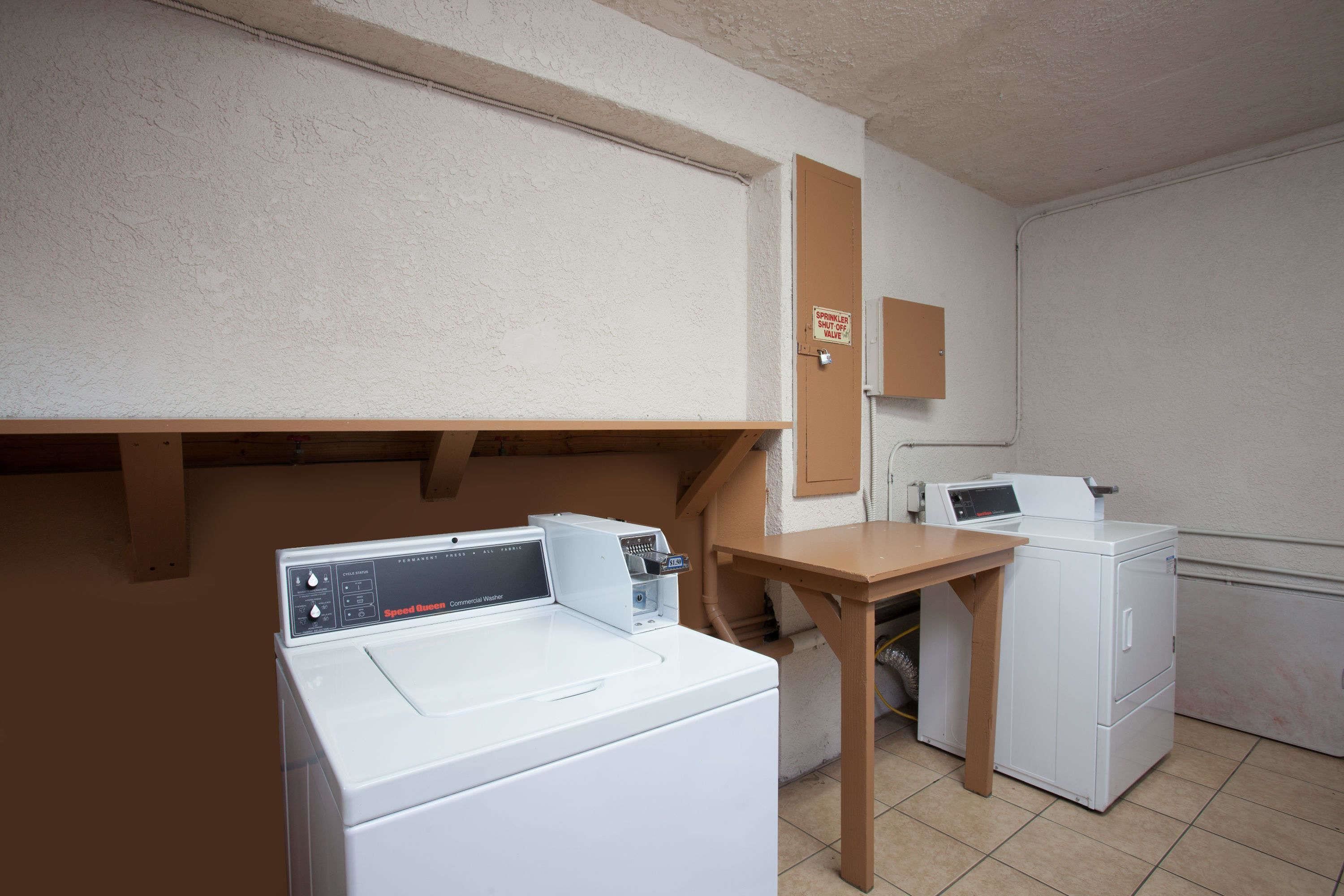A laundry room with a front-loading washer and dryer, a wooden table, and a door with a sign.