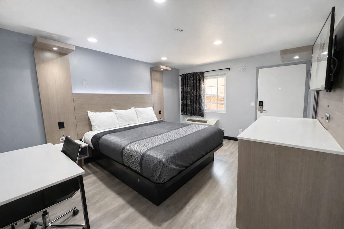 A hotel room with a bed, a desk, a chair, a bathroom, and a TV.