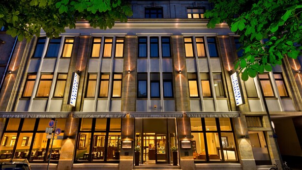 Et hotel med en moderne facade, store vinduer og oplyst skiltning.