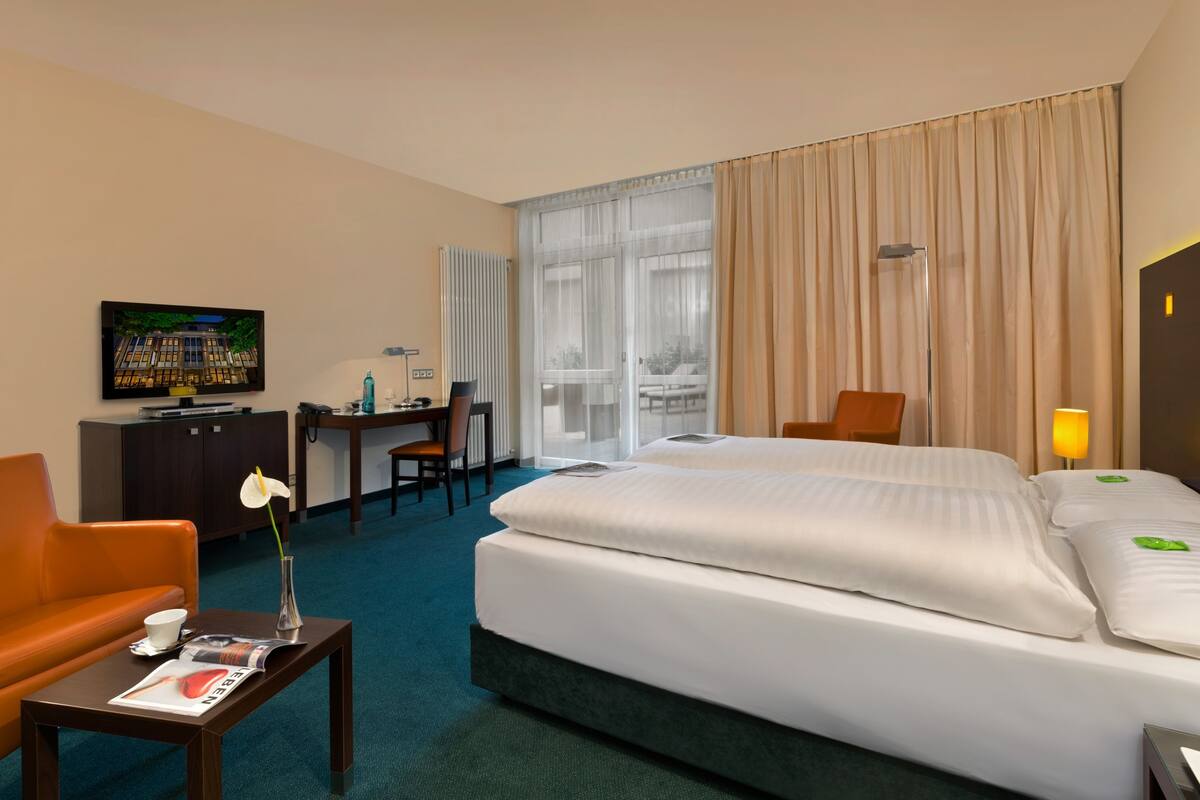 Habitación de hotel con una cama grande, un escritorio, una silla, un televisor y una ventana con cortinas.