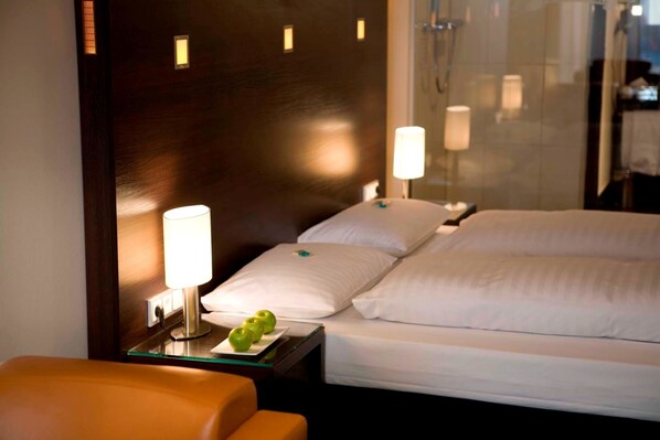 Habitación de hotel con cama, lámparas de noche, una mesita con manzanas y un separador de vidrio.