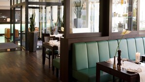 En restaurant med grønne polstrede bænke, træborde og krukkeplanter.