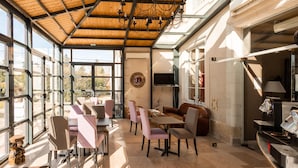 A spacious indoor area with large windows, a wooden ceiling, and a seating arrangement including tables and chairs.