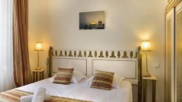Una camera d'albergo con un letto rifatto, due abat-jour, un quadro incorniciato al muro e una finestra con tende.