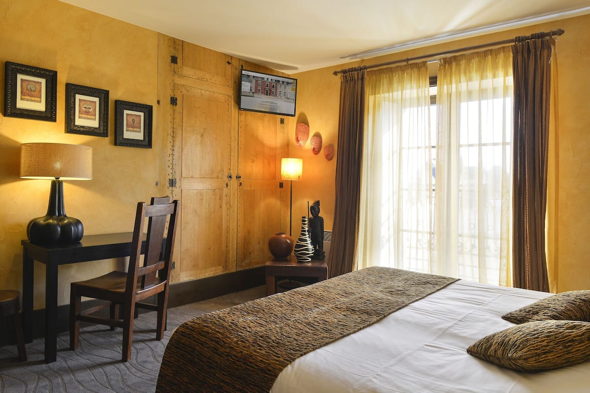 Hotelkamer met een bed, een bureau met stoel, een lamp, een fotolijst en een raam met gordijnen.