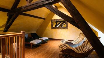 A room with a sloped ceiling, wooden beams, a hammock, and two lounge chairs.