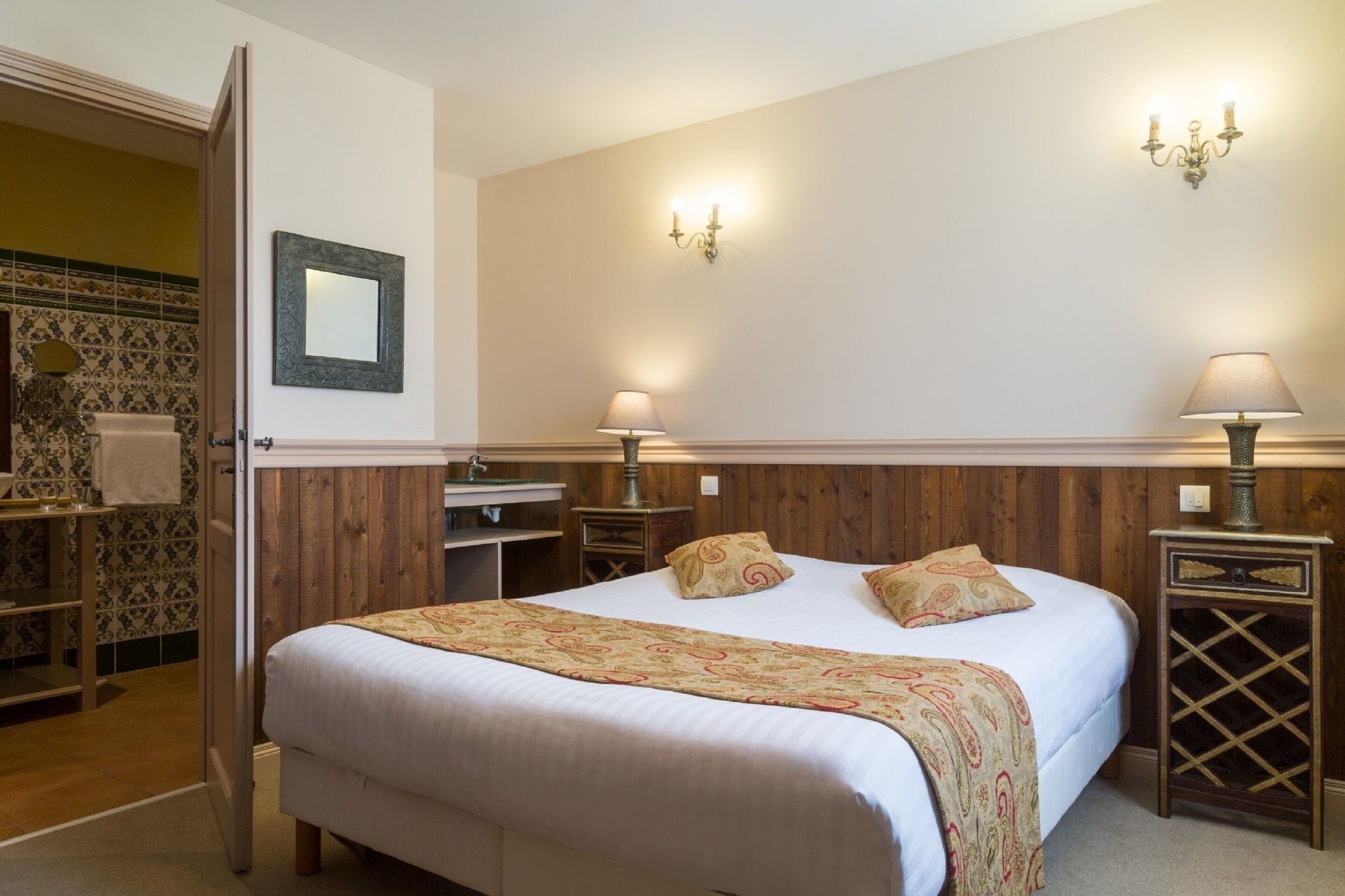 Un dormitorio con una cama grande, dos mesitas de noche con lámparas, un espejo en la pared y un armario de madera.