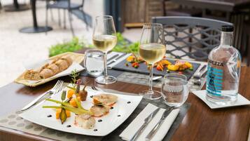 Una mesa de comedor con platos de comida, copas de vino blanco y una botella de agua.