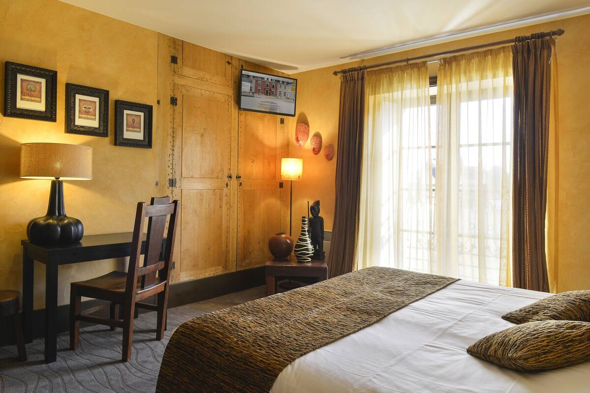 Een hotelkamer met een bed, een bureau, een stoel, een lamp en een raam met gordijnen.