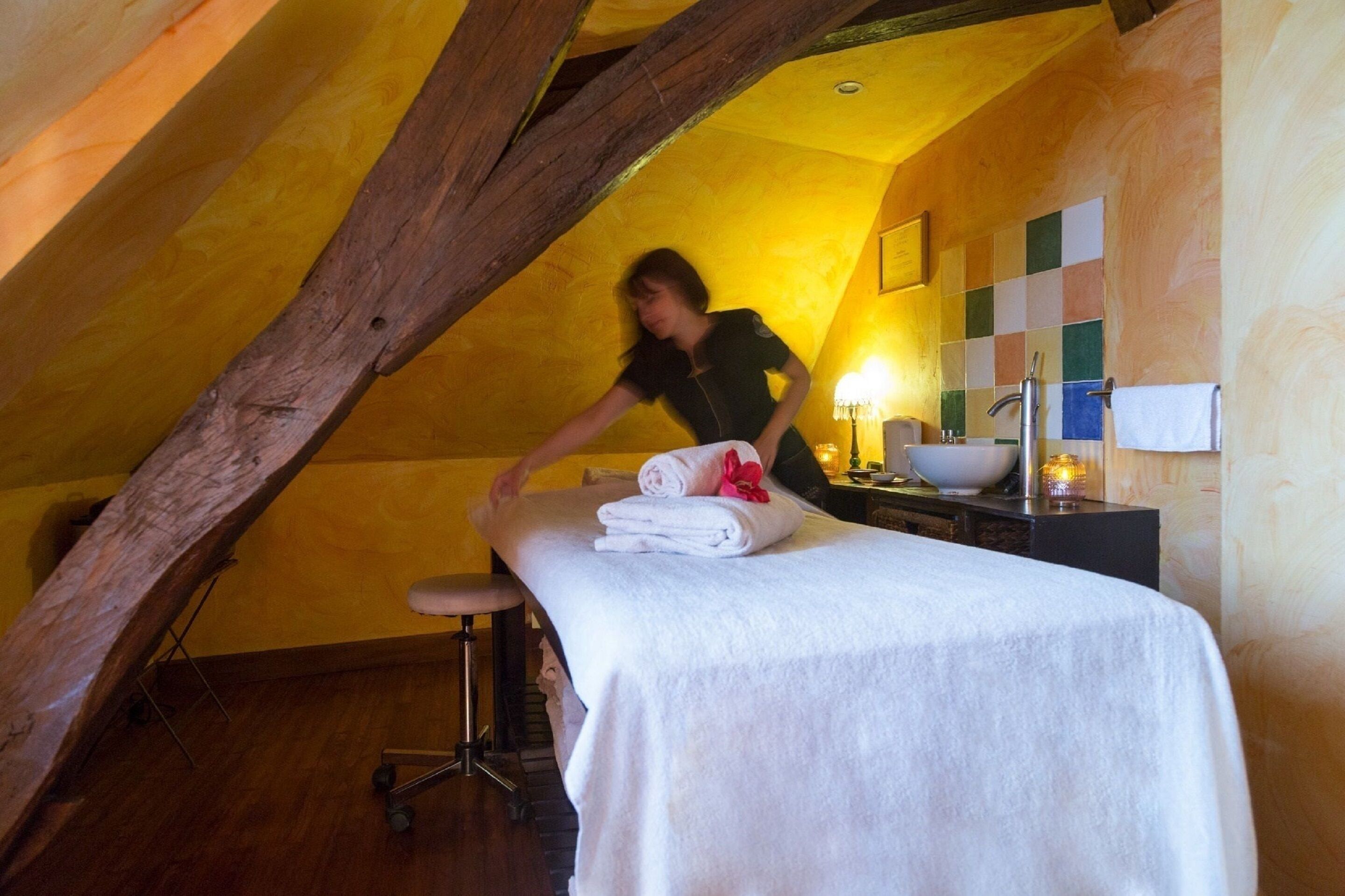 Une pièce avec un plafond en bois, une table de massage avec des serviettes, un petit tabouret et un lavabo fixé au mur.