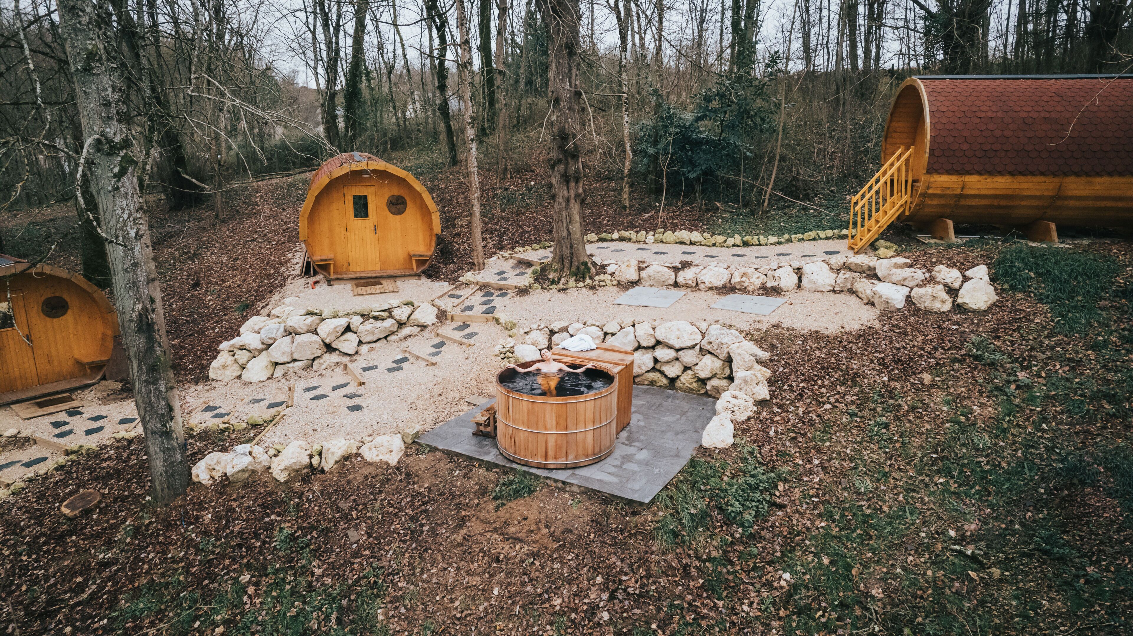 A forest setting with wooden cabins, a sauna, and a stone pathway.