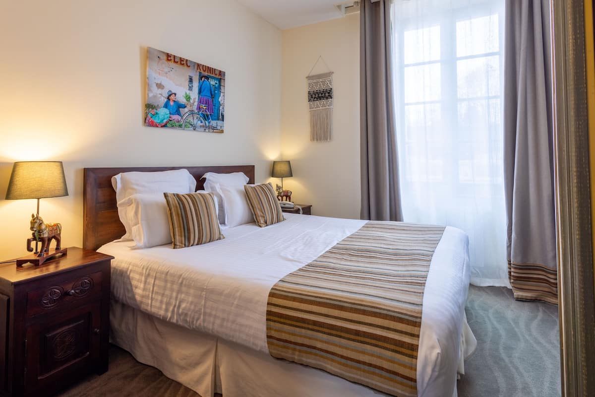 Hotelkamer met een groot bed, twee nachtkastjes met lampen, een macramé wanddecoratie en een raam met gordijnen.
