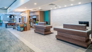 A modern reception area with wooden reception desks, a hexagonal tiled floor, and a wavy textured wall. - Hilton Garden Inn Augusta (Augusta)