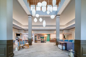 A spacious lobby with a reception desk, seating area, and a shop in the background. - Hilton Garden Inn Augusta (Augusta)