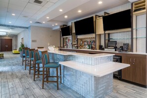 A modern kitchen with a bar area, bar stools, and a flat-screen TV mounted above the bar. - Hilton Garden Inn Augusta (Augusta)
