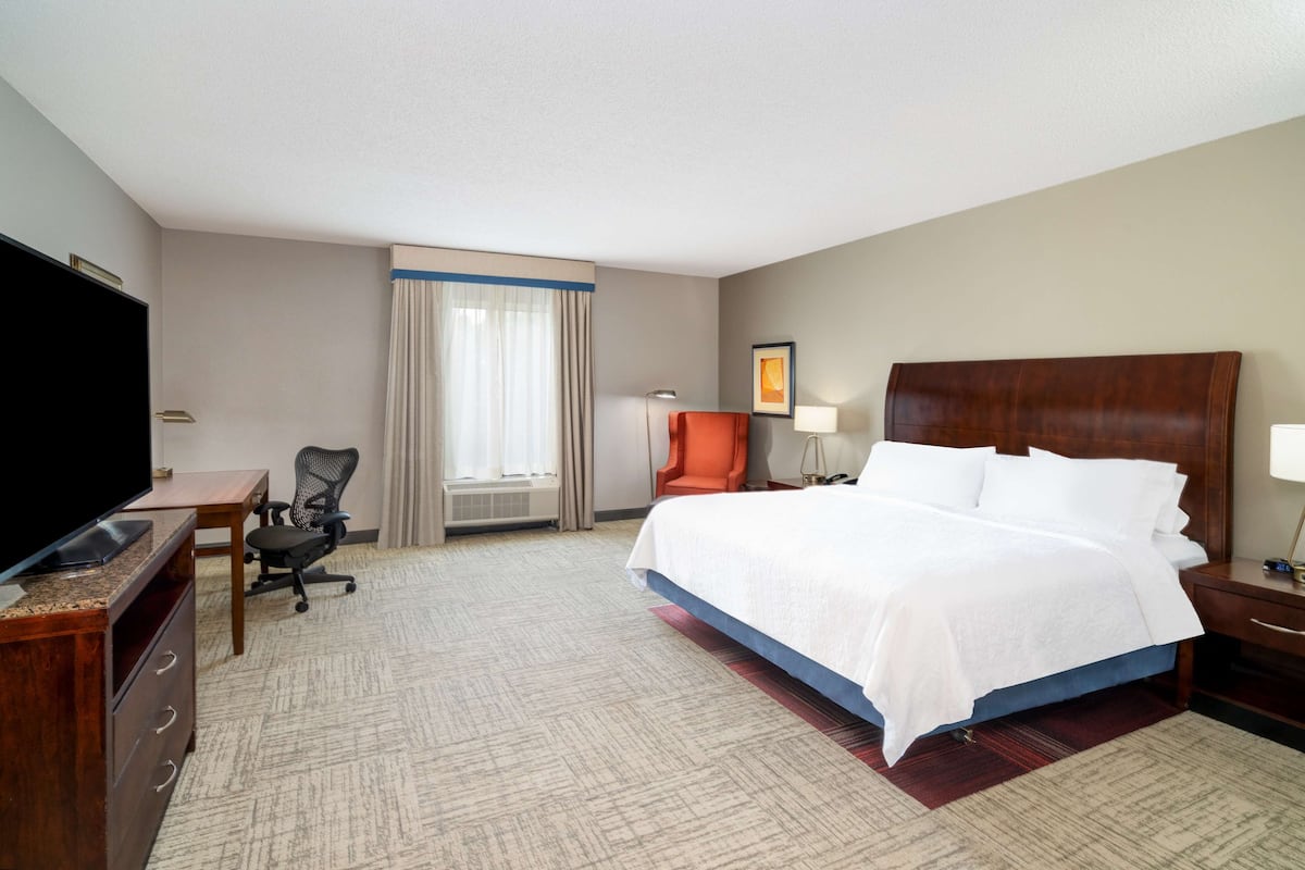 Quarto de hotel com cama grande, escrivaninha com televisão de tela plana, cadeira e janela com cortinas.
