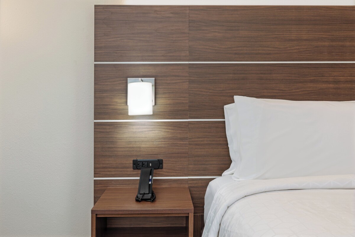 Una habitación de hotel moderna con un cabecero de madera, una mesita de noche con lámpara y una cama bien hecha.