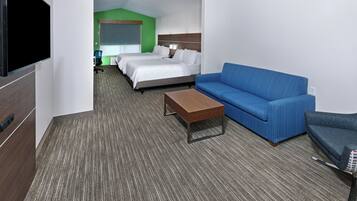 A hotel room with a bed, a blue sofa, a wooden coffee table, and a television.