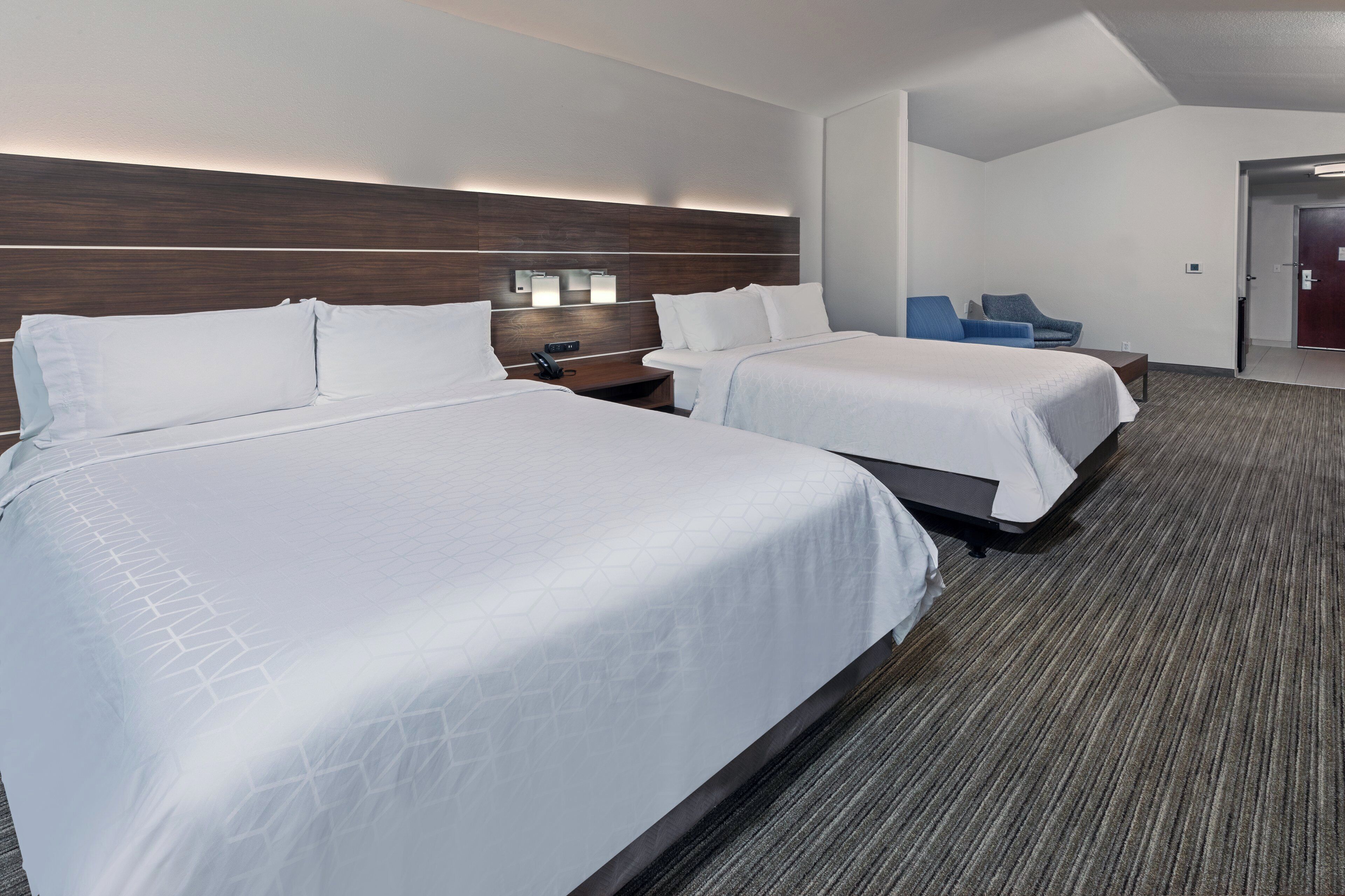 A hotel room with two beds, a nightstand, a desk, and a chair.