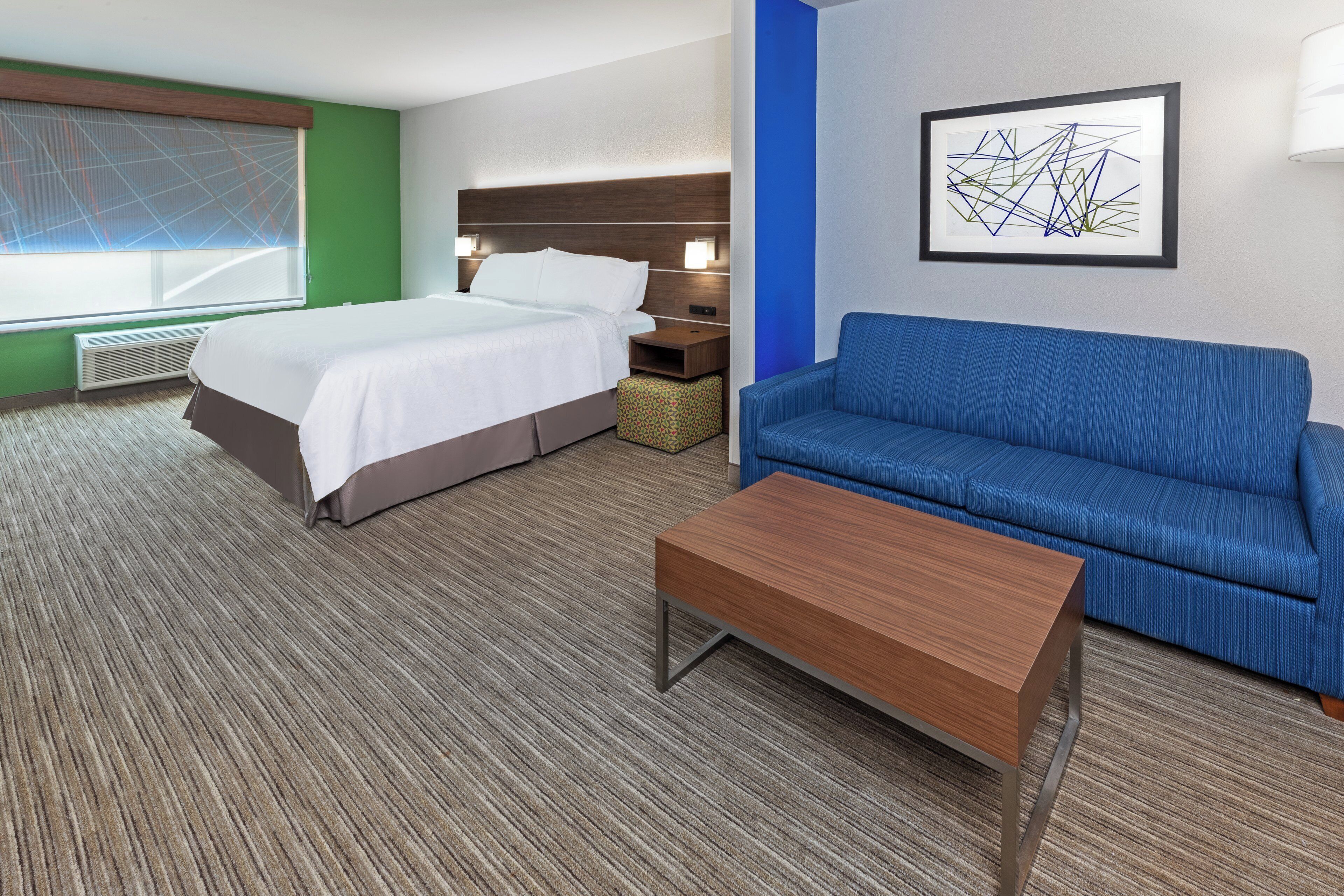 A hotel room with a bed, a blue sofa, a wooden coffee table, and a wall-mounted artwork.