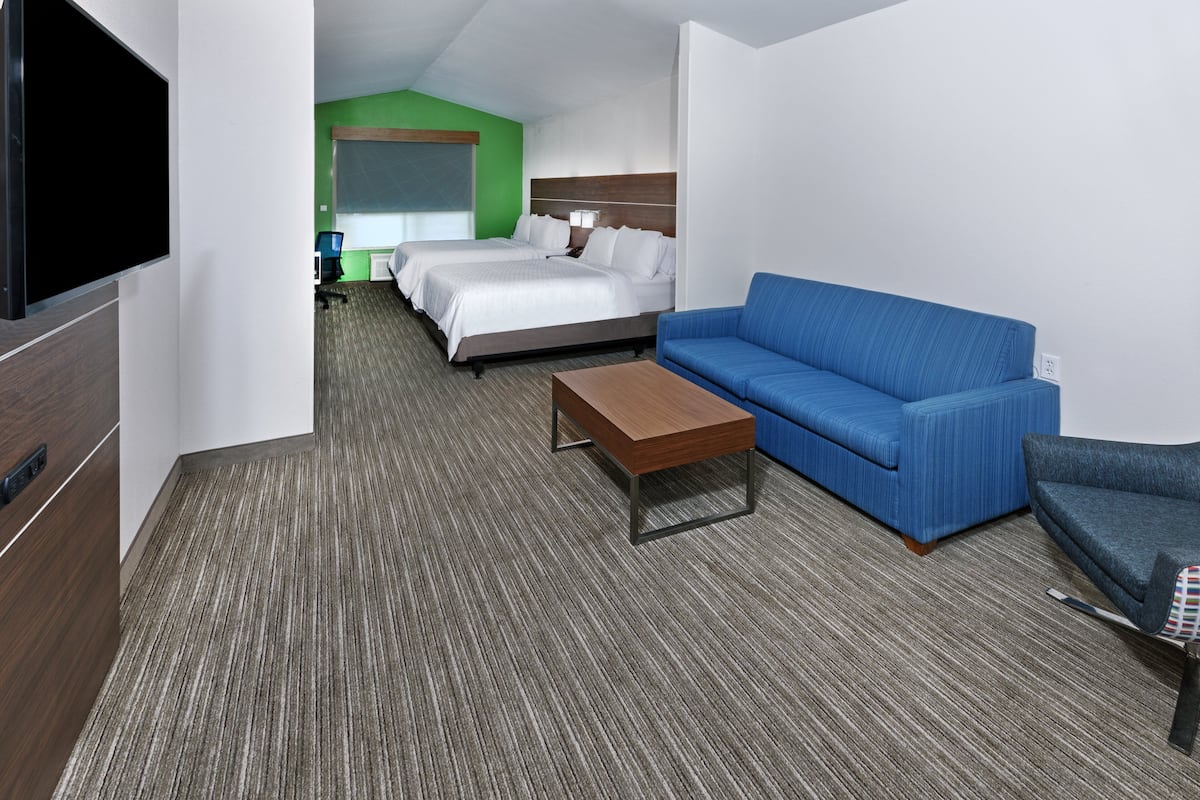 A hotel room with a bed, a blue sofa, a wooden coffee table, and a TV.