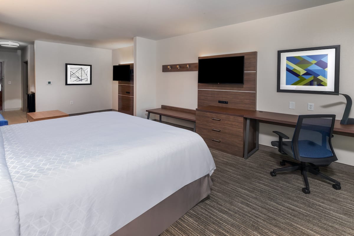 A hotel room with a large bed, a desk with a chair, a flat-screen TV, and artwork on the walls.