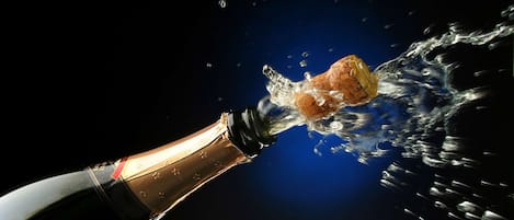 A bottle of champagne being opened, with a cork being ejected into a splash of liquid.