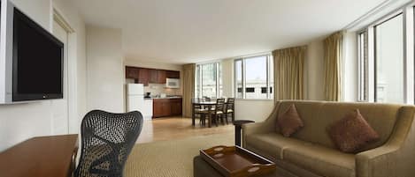 A modern hotel room with a living area, kitchenette, and a large window offering a city view.