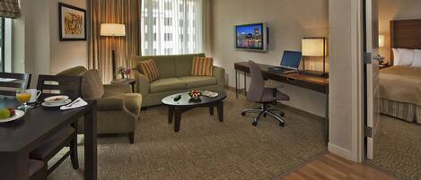 A hotel room with a sofa, a dining table with breakfast, a desk with a laptop, and a bed.