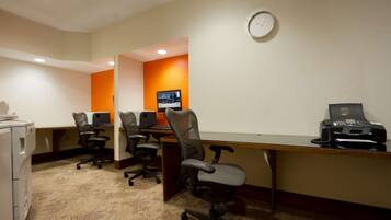 A conference room with desks, chairs, a clock, and a printer.