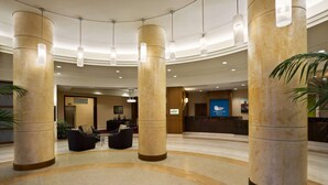 Eine großzügige Lobby mit hohen Säulen, einer Rezeption und Sitzbereichen.