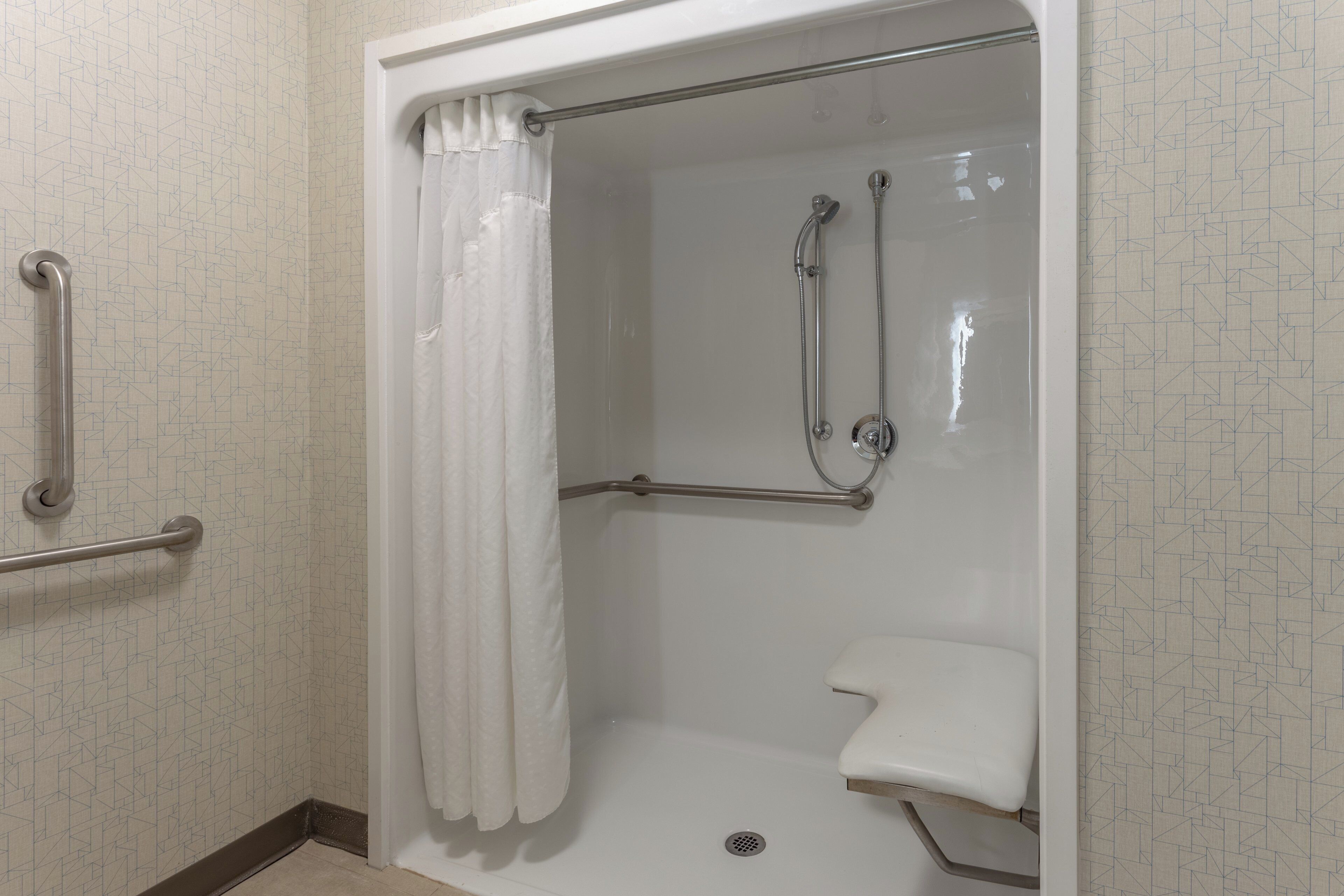 A shower stall with a grab bar, a showerhead, and a white curtain.