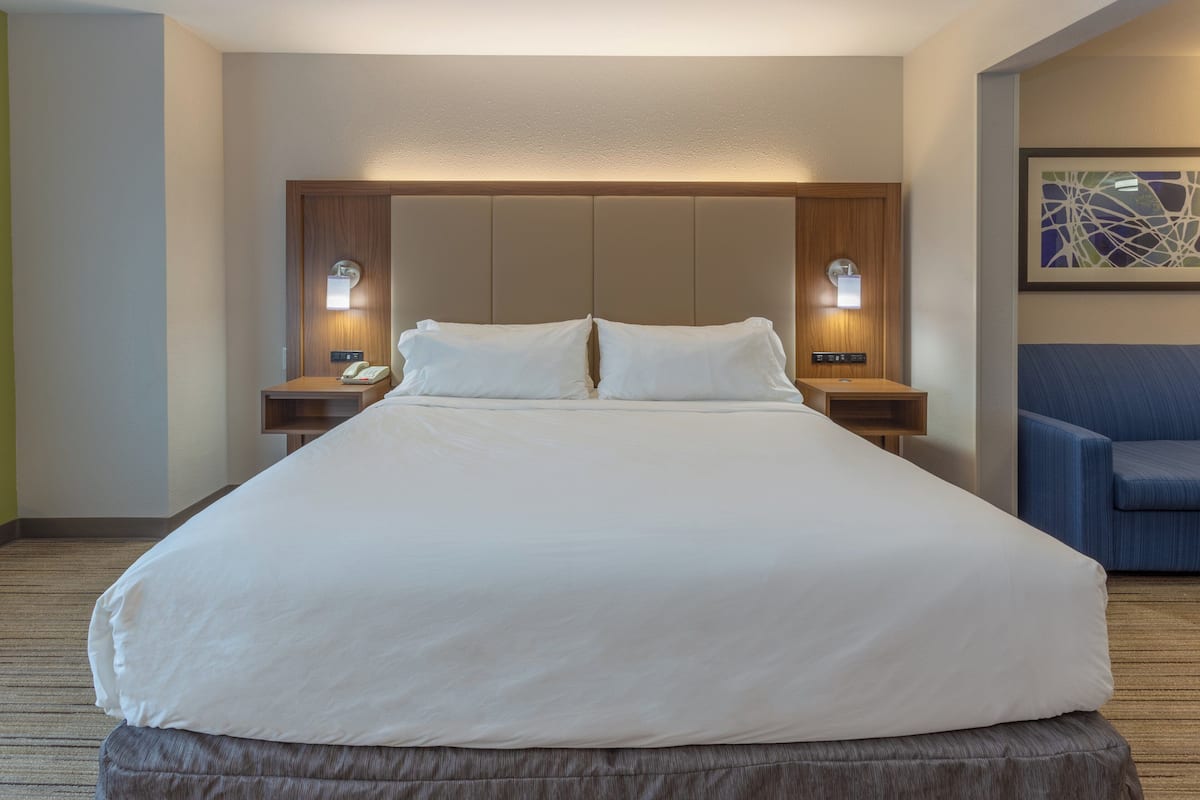 A large bed with a wooden headboard, two bedside tables with lamps, and a blue chair.