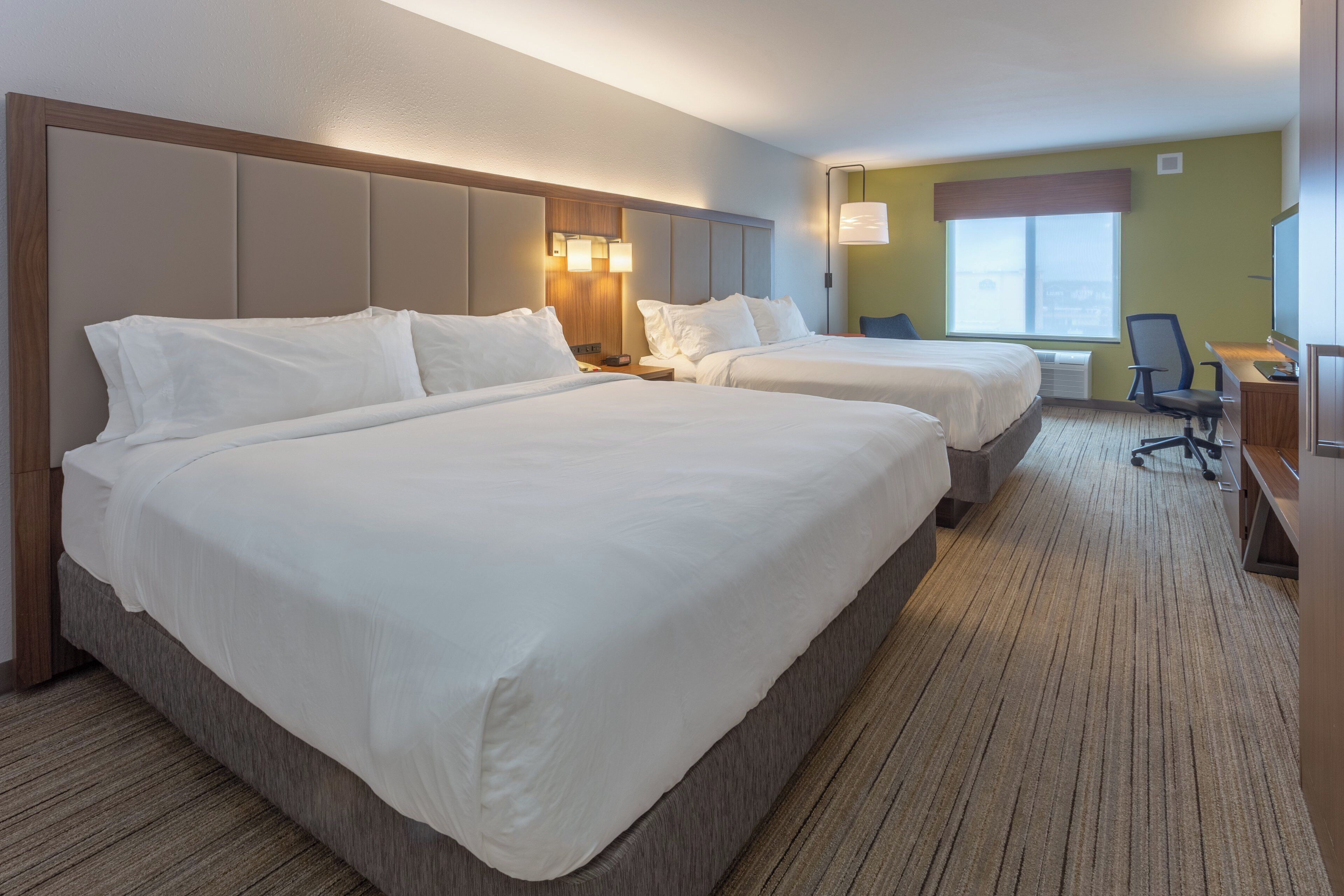 Habitación de hotel con dos camas, un escritorio, una silla y una ventana.