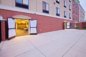 A hotel entrance with a brick facade, open doors leading to a dining area, and a gated parking area. - Holiday Inn Express Indianapolis - Southeast by IHG (Indianapolis)