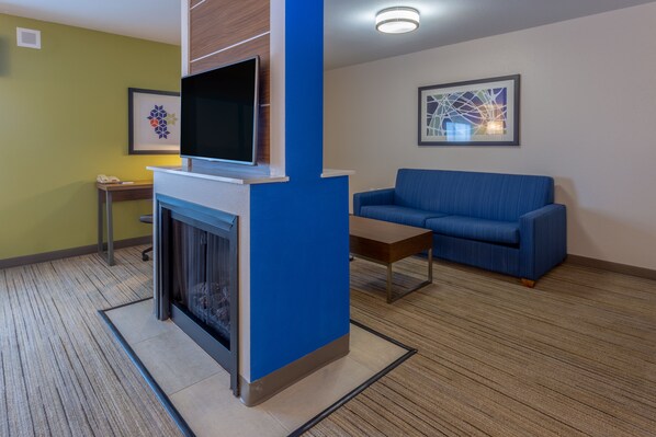 A modern living room with a fireplace, a blue sofa, and a flat-screen TV mounted on a wooden wall. - Holiday Inn Express Indianapolis - Southeast by IHG (Indianapolis)
