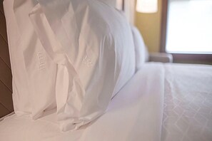 A neatly made bed with white linens and pillows, a wooden headboard, and a window in the background. - Holiday Inn Express Indianapolis - Southeast by IHG (Indianapolis)