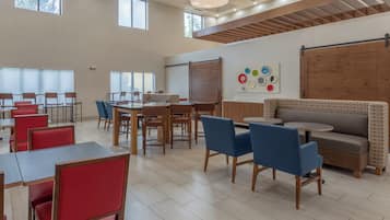 Un comedor espacioso con techos altos, ventanas grandes y una mezcla de asientos rojos y azules.