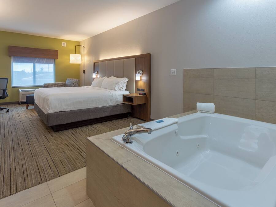 Ein Hotelzimmer mit einem großen Bett, einem separaten Schreibtisch mit Stuhl, einer Schreibtischlampe, einem Fenster mit Aussicht und einem eigenen Badezimmer mit Badewanne.