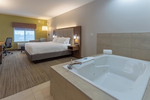 Quarto de hotel com uma cama grande, uma mesa de trabalho separada com cadeira, luminária de mesa, janela com vista e banheiro privativo com banheira.
