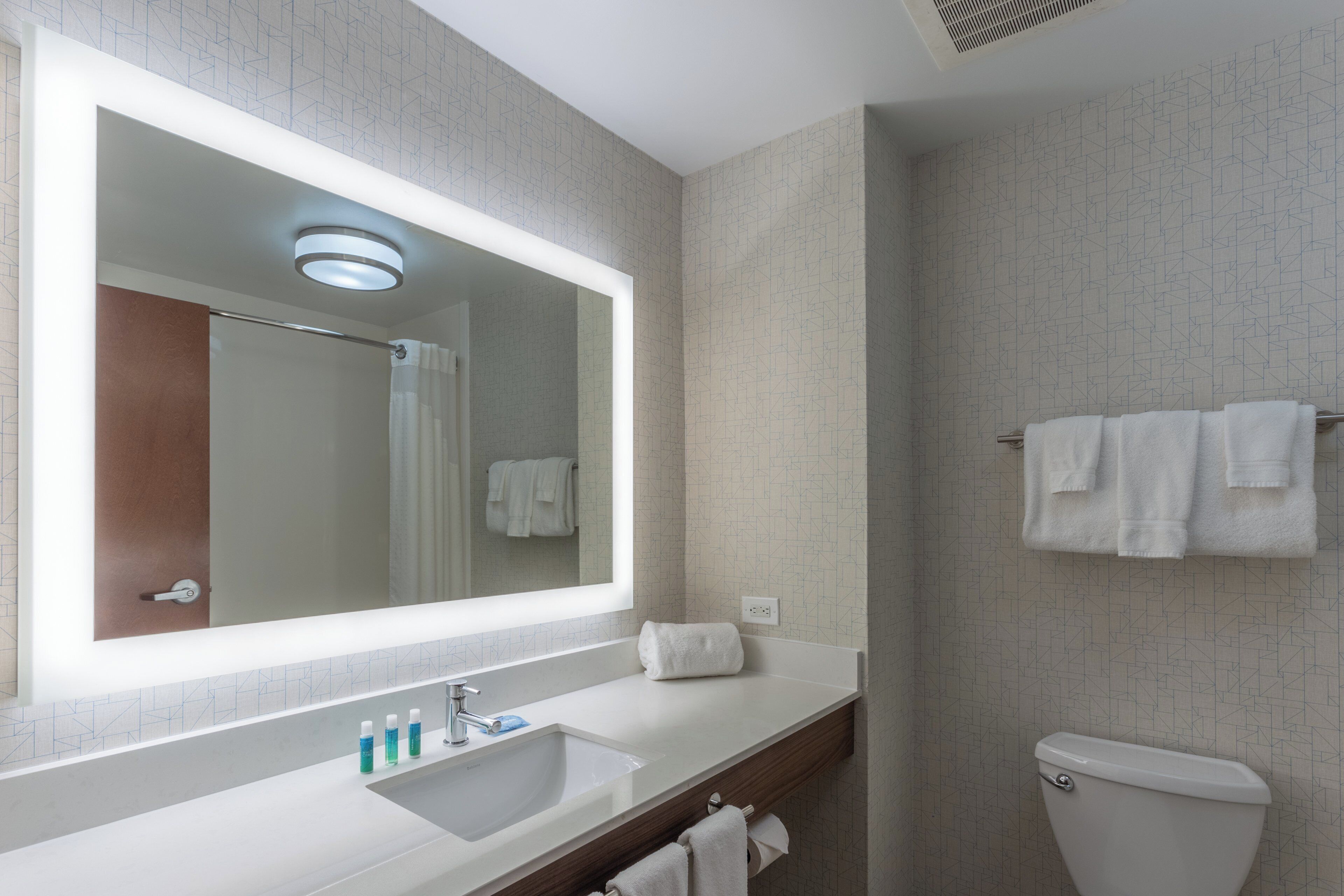 A bathroom with a large mirror, a sink, a toilet, and a towel rack.
