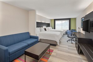 A hotel room with a blue sofa, two beds, a desk with a chair, a television, and a large window. - Holiday Inn Express & Suites Pembroke Pines-Sheridan St by IHG (Pembroke Pines)