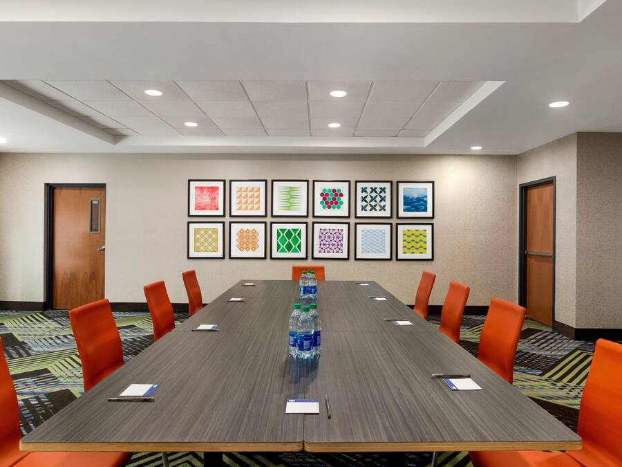 A conference room with a long table, orange chairs, and framed artwork on the wall.