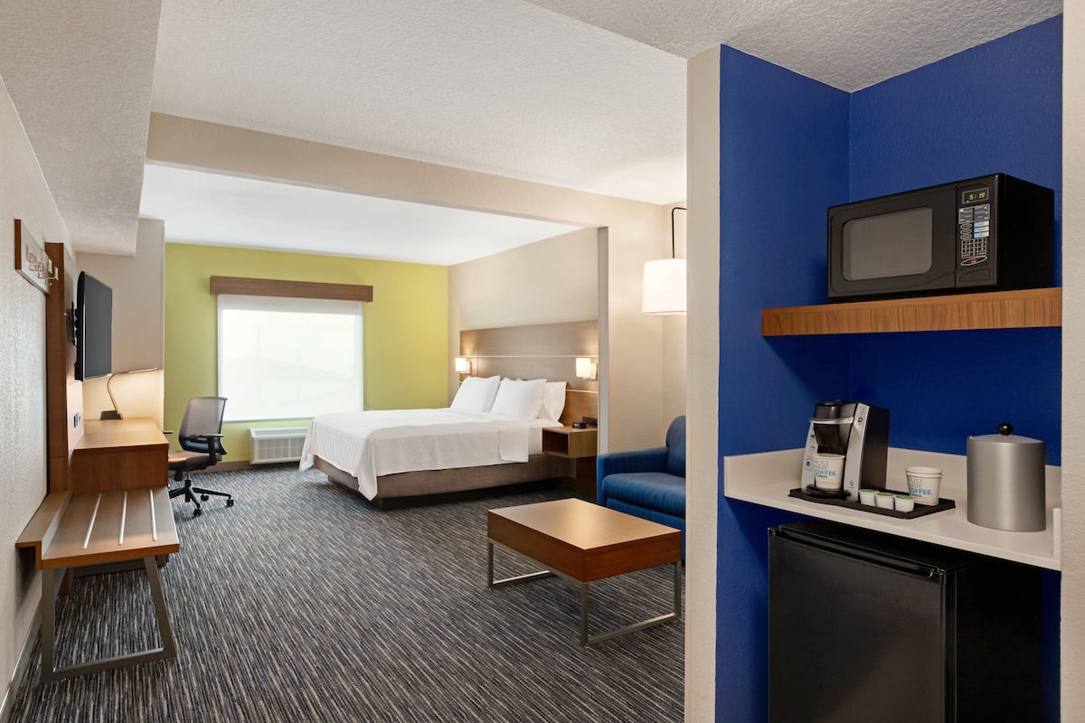 A hotel room with a bed, a desk, a chair, a coffee machine, and a microwave.